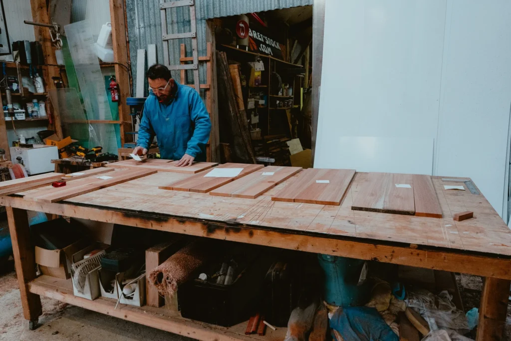 Vue large de l’atelier KoadBooth : un menuisier travaille à l’établi au milieu des planches