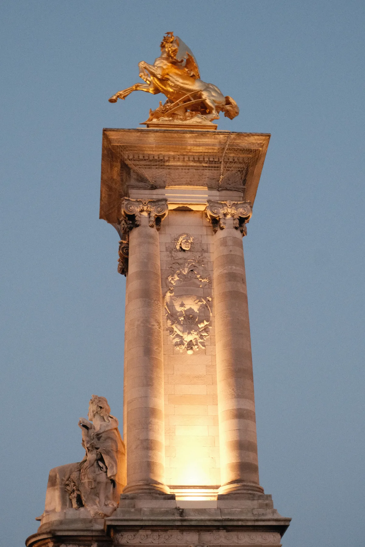 Statue dorée surmontant une colonne de pont, éclairée au crépuscule, en Île-de-France