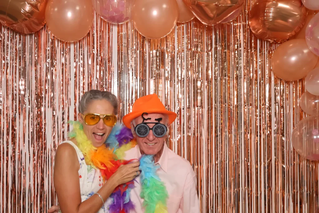 Un couple de seniors pose avec un chapeau orange, des lunettes fantaisie et un boa multicolore