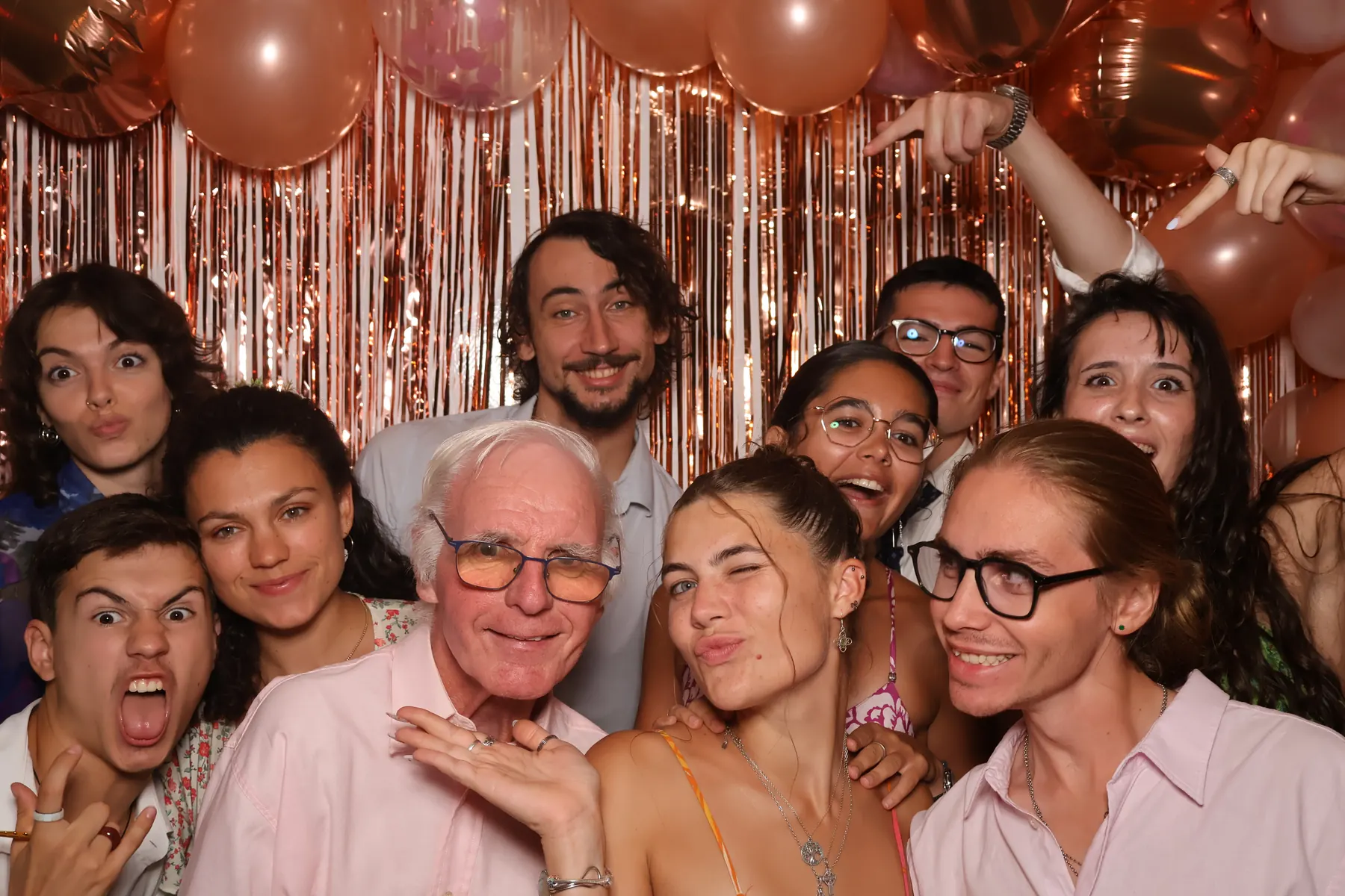 Une dizaine d'invités de mariage se serrent dans le champ du photobooth devant le fond à franges cuivrées.
