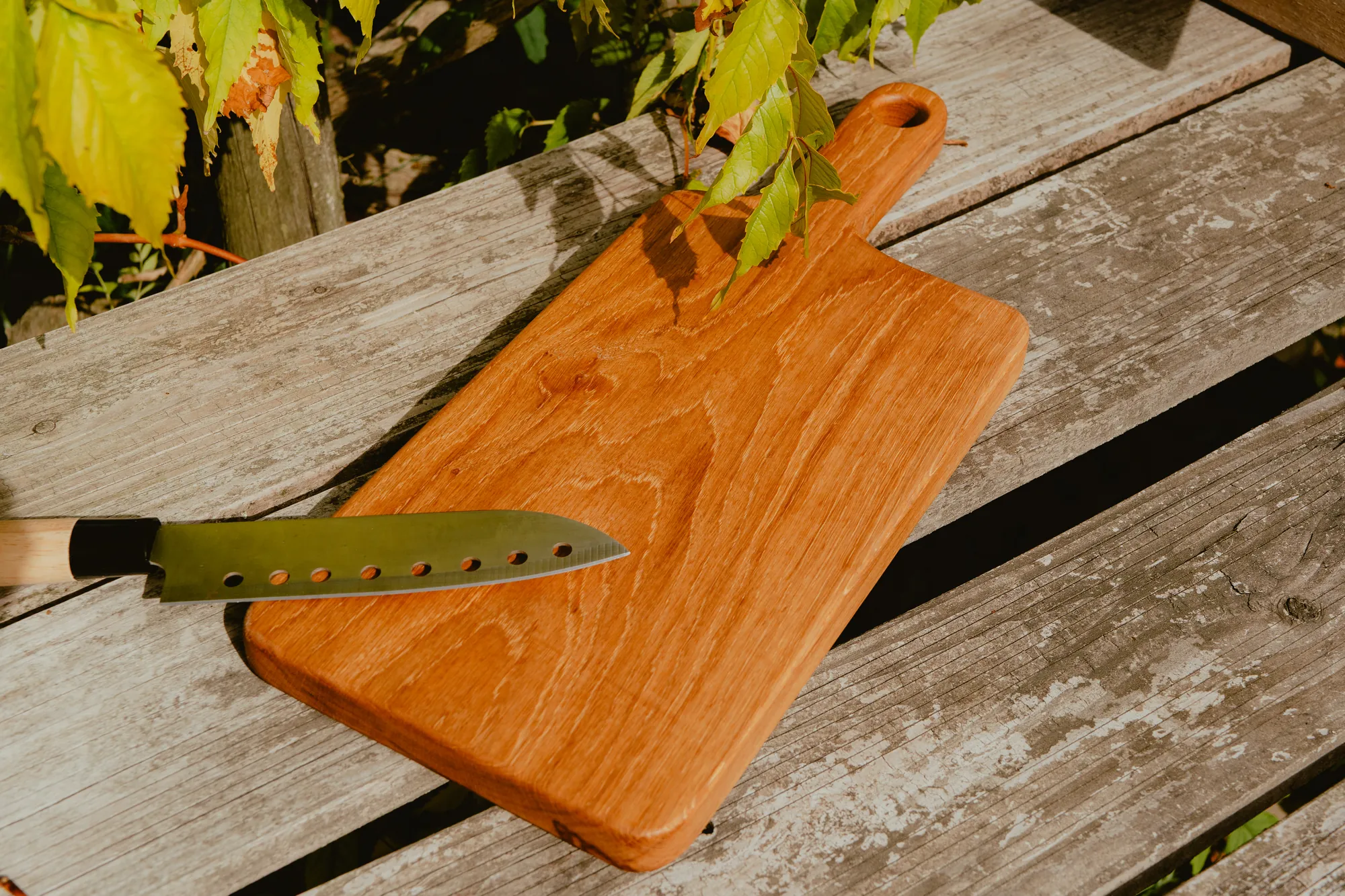 Planche de service longue en bois huilé, un couteau posé dessus.